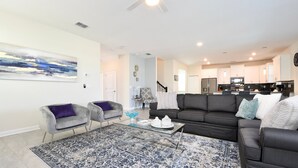 A modern living room with a sectional sofa, two armchairs, a glass coffee table, and a large abstract painting on the wall. - Modern Oasis Near Shopping n Golf Course w Pool (Davenport)