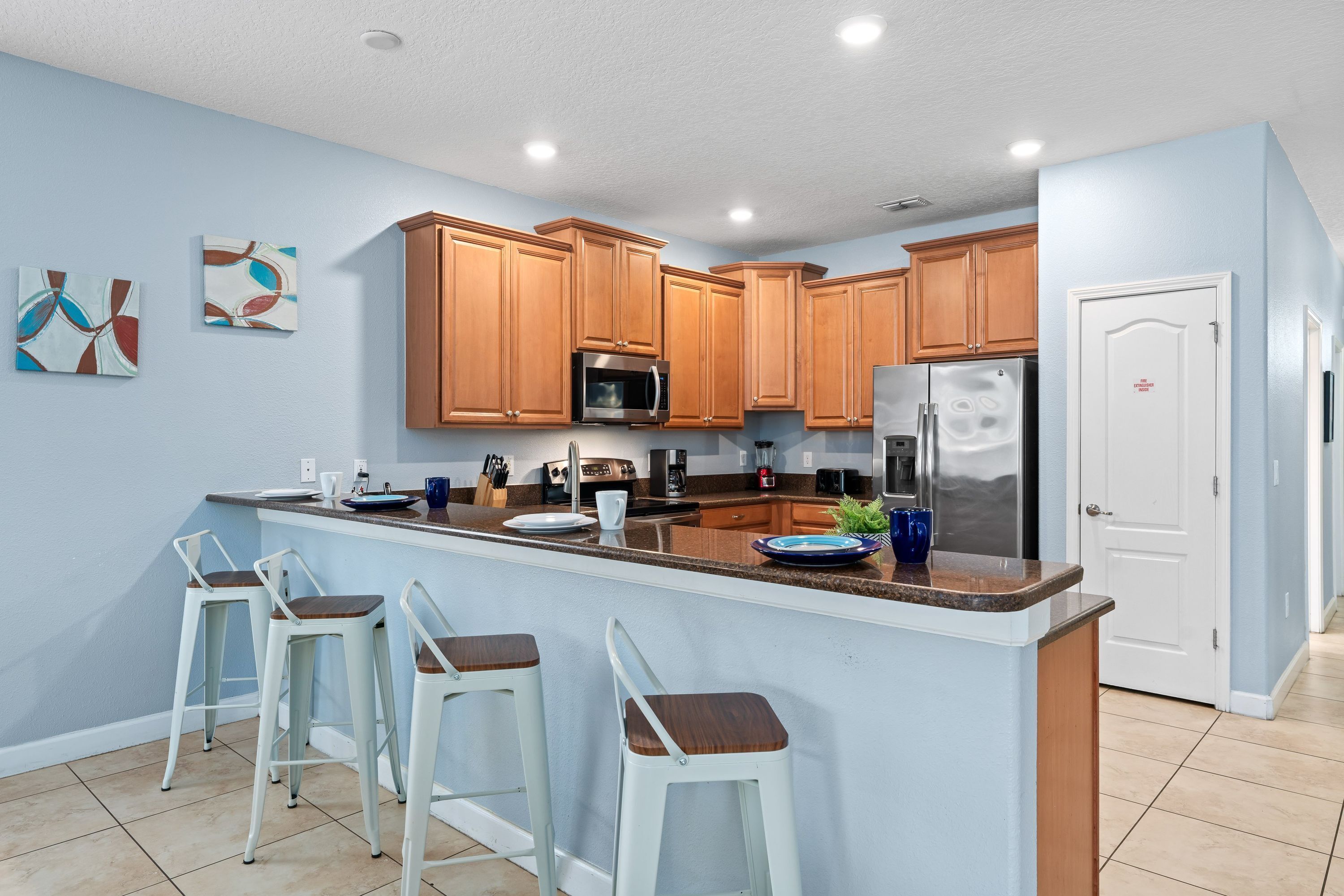 A modern kitchen with wooden cabinets, a stainless steel refrigerator, and a bar area with stools.