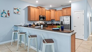 Une cuisine moderne avec des meubles en bois, un réfrigérateur en acier inoxydable et un coin bar équipé de tabourets.