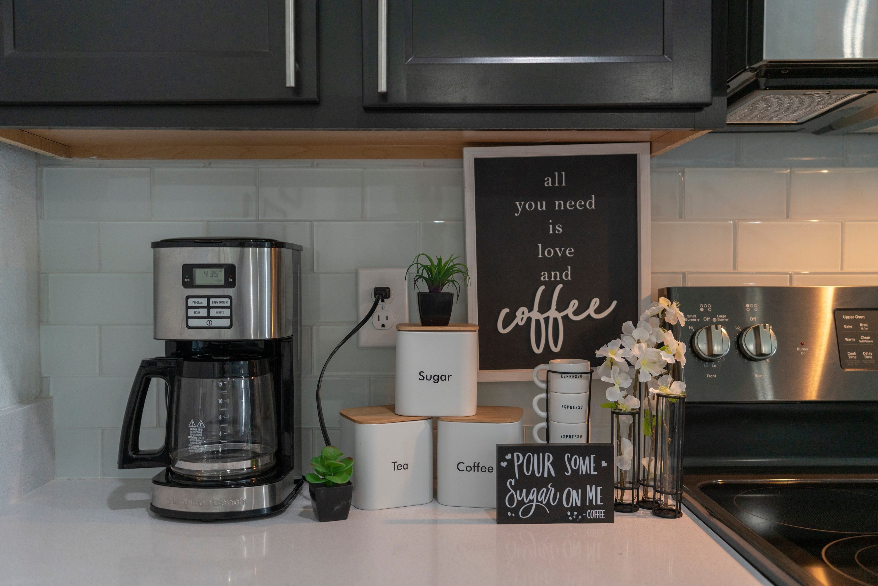A kitchen counter with a coffee maker, sugar, tea, and coffee containers, and a sign that says "all you need is love and coffee."