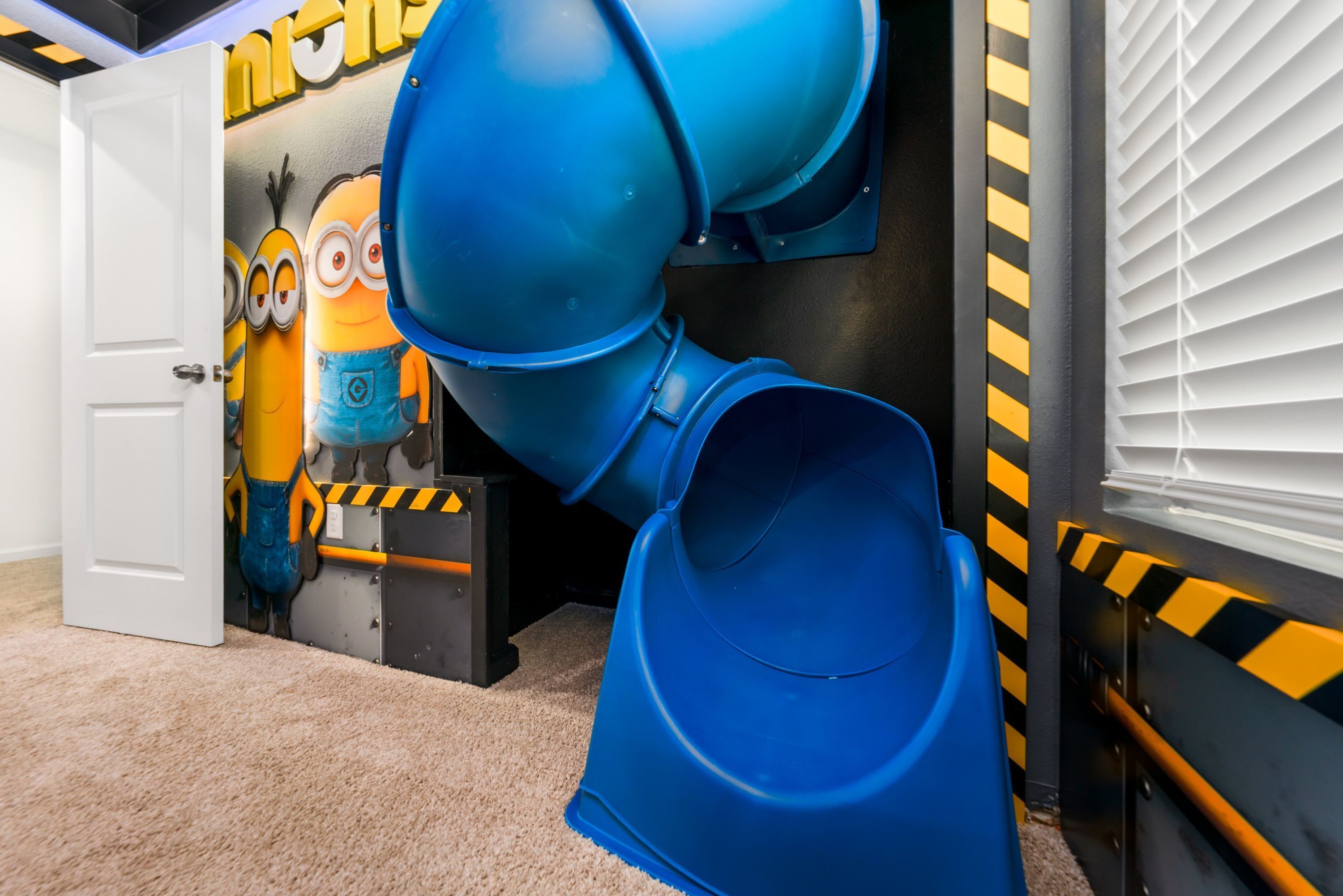 Una stanza con uno scivolo blu, una porta e un muro decorato con i personaggi dei Minions.