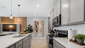 A modern kitchen with grey cabinets, a stainless steel microwave, and a large island with a sink. - Perfect for Children With Epic Themed Bedrooms (Kissimmee)