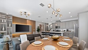 A modern kitchen with a central island, built-in appliances, and a dining area with a wooden table and chairs. - Perfect for Children With Epic Themed Bedrooms (Kissimmee)
