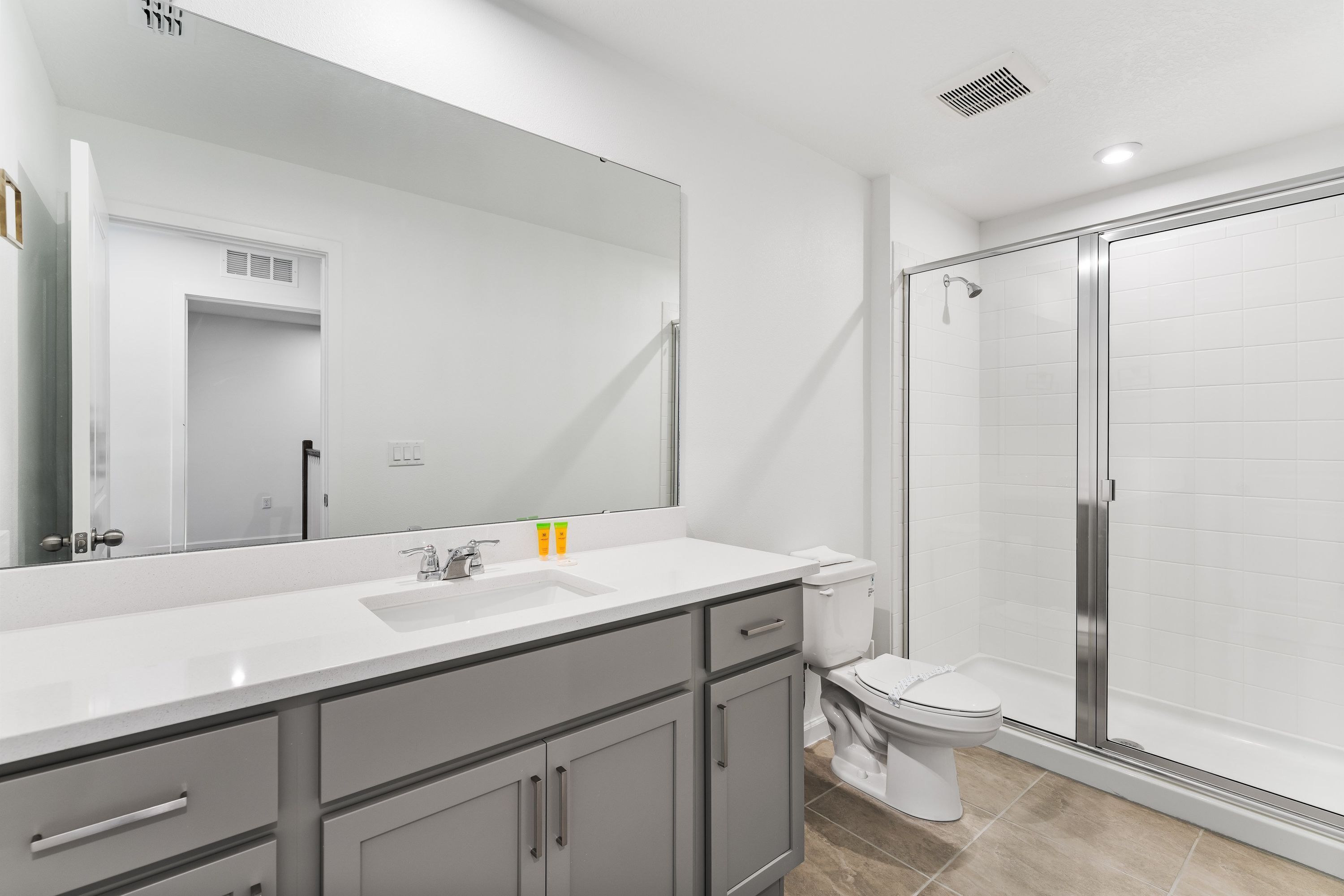 A modern bathroom with a large mirror, white sink, and a walk-in shower.