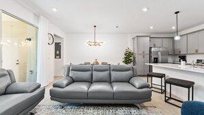 Una sala de estar moderna con un sofá gris, una mesa de centro y un comedor con una araña.