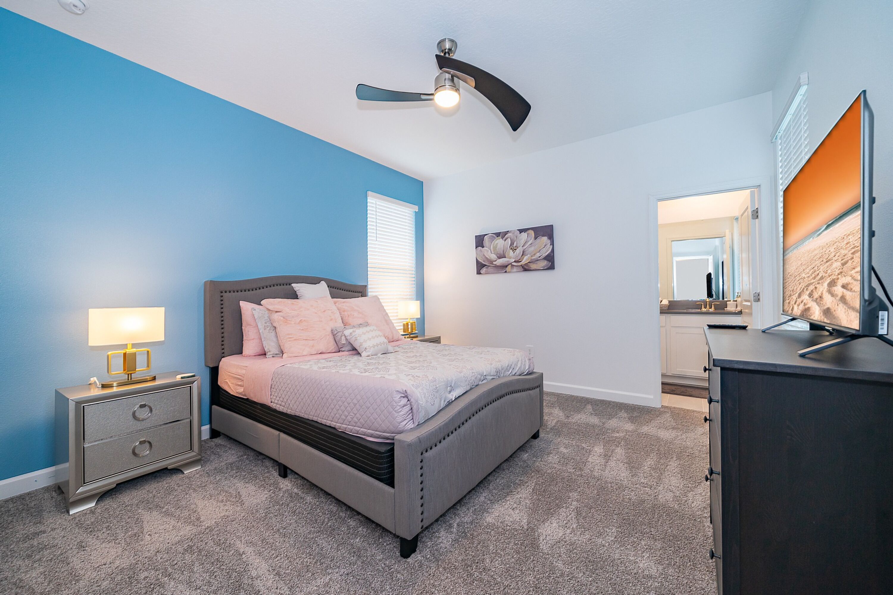A bedroom with a bed, nightstand, dresser, ceiling fan, and artwork.
