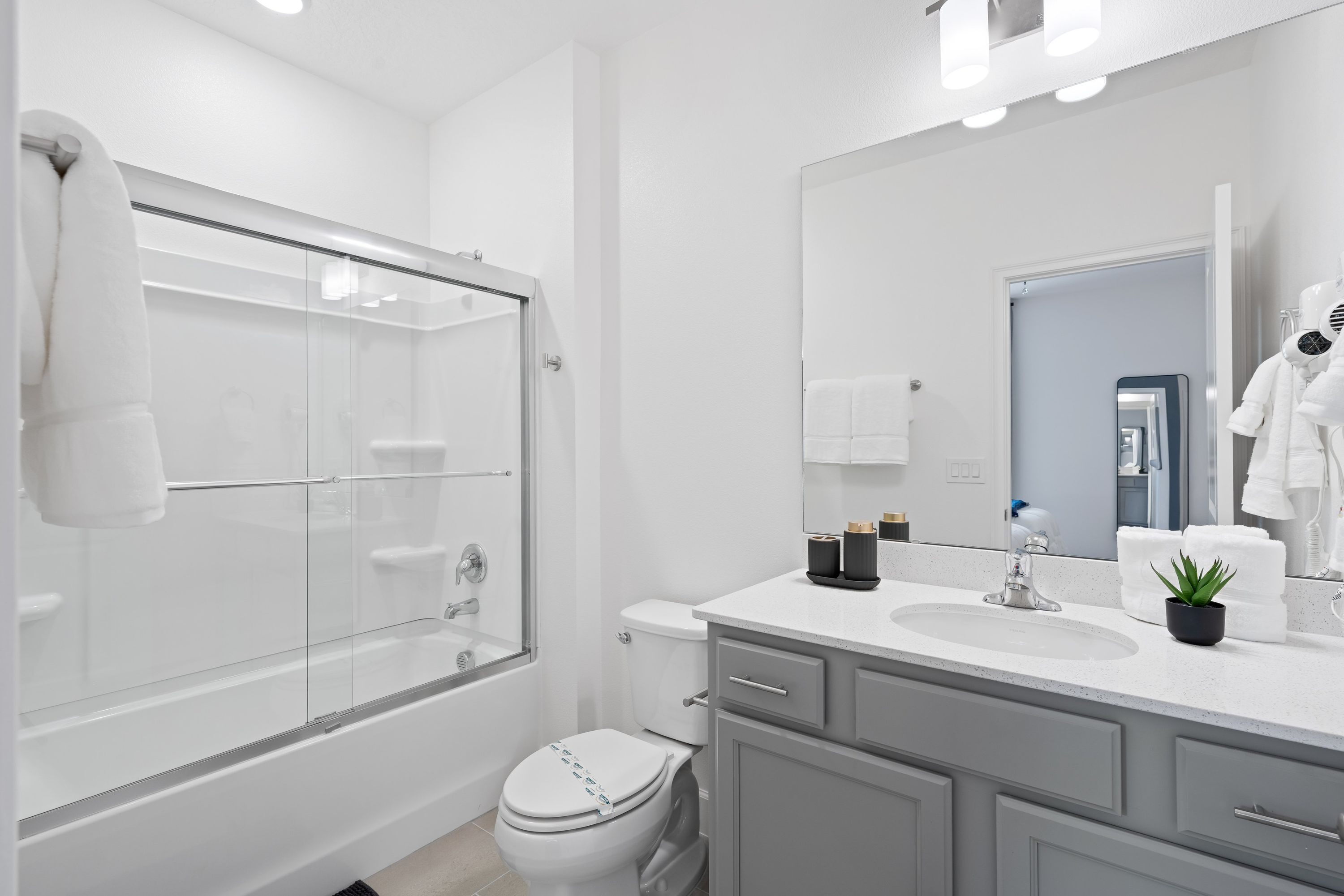 Une salle de bain moderne avec une douche à parois de verre, des toilettes blanches, un meuble-lavabo et un grand miroir.