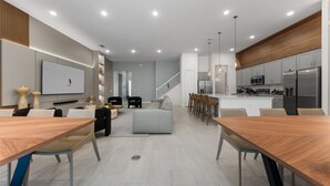 A modern kitchen with stainless steel appliances, a dining area with a wooden table, and a living space with a sofa and TV. - Brand New Modern State of the Art Home Sleeps 31 (Kissimmee)