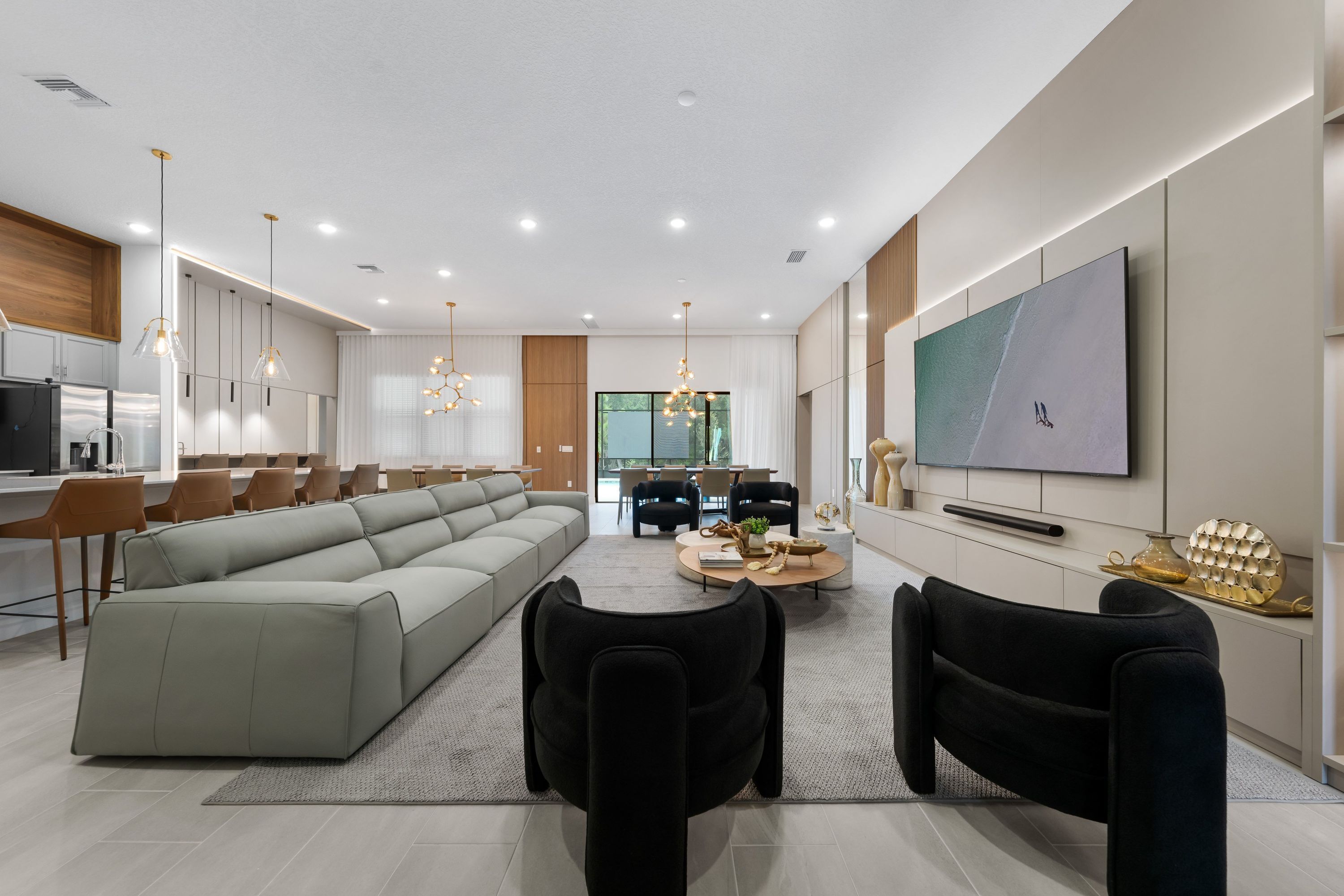 A modern living room with a sectional sofa, black chairs, a coffee table, and a TV mounted on the wall.