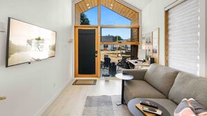 Ett modernt vardagsrum med ett stort fönster, en soffa, ett soffbord och en tv som hänger på väggen.