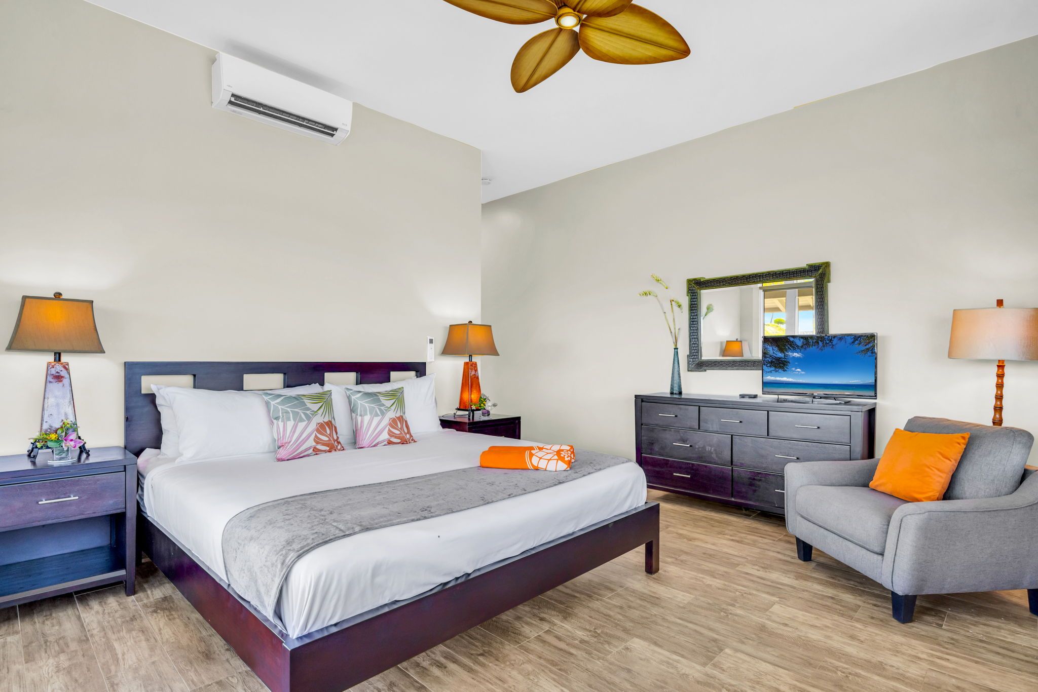 Ein Hotelzimmer mit Bett, Nachttischen, einem Schminktisch, einem Sessel, einem Deckenventilator, einem Fernseher und einem Spiegel.
