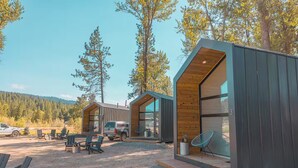 Une cabane moderne dotée d’un patio en gravier, d’un espace salon extérieur et d’un camion garé à proximité.