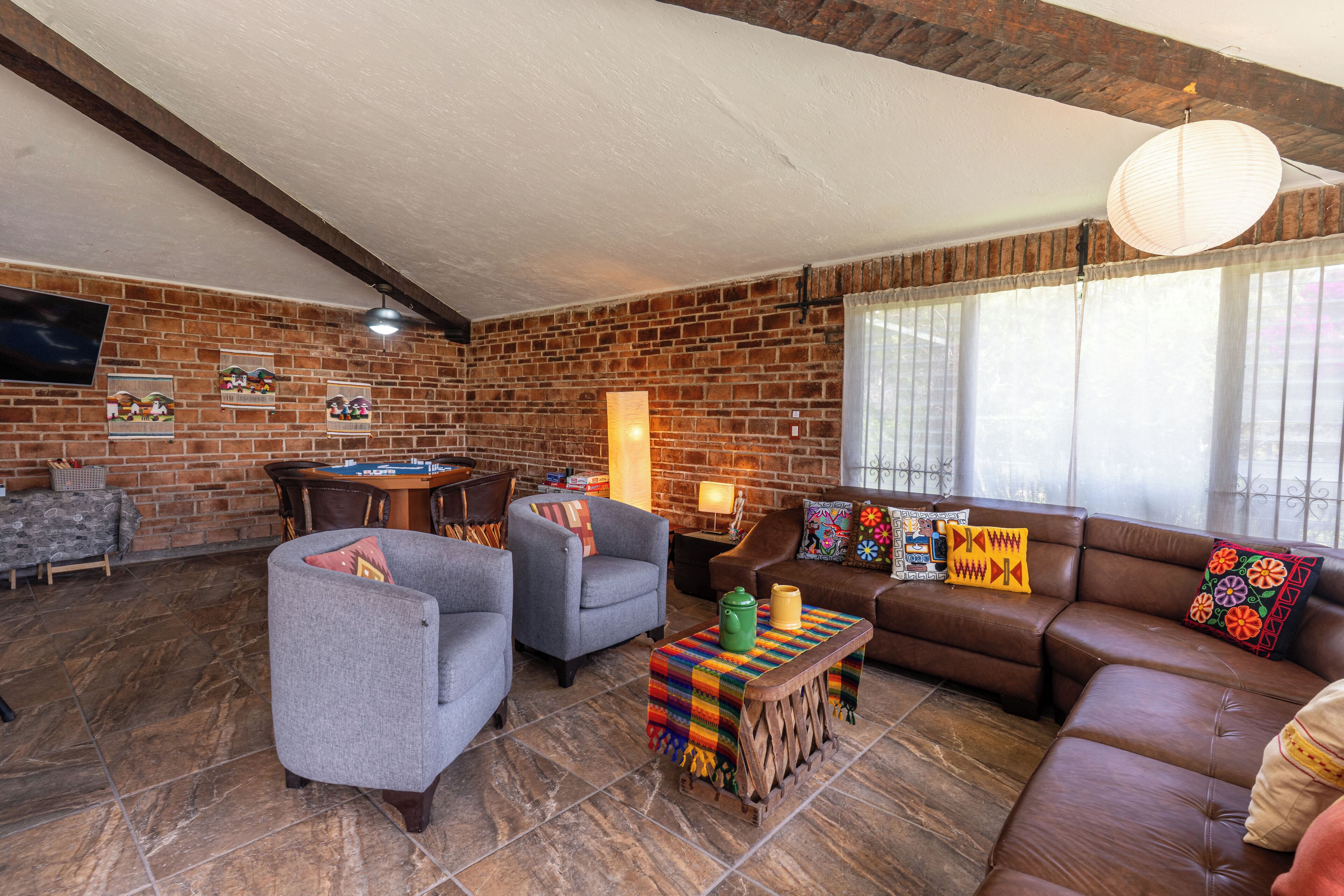 A cozy living room with brick walls, a brown leather sofa, two armchairs, a coffee table, and a television on the wall.