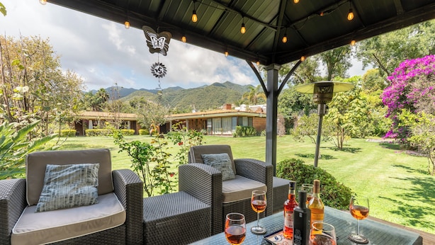 Un espace extérieur aménagé avec des meubles en osier, une table en verre et des verres à vin.