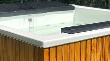 A hot tub with a wooden exterior and a glass top, surrounded by greenery.