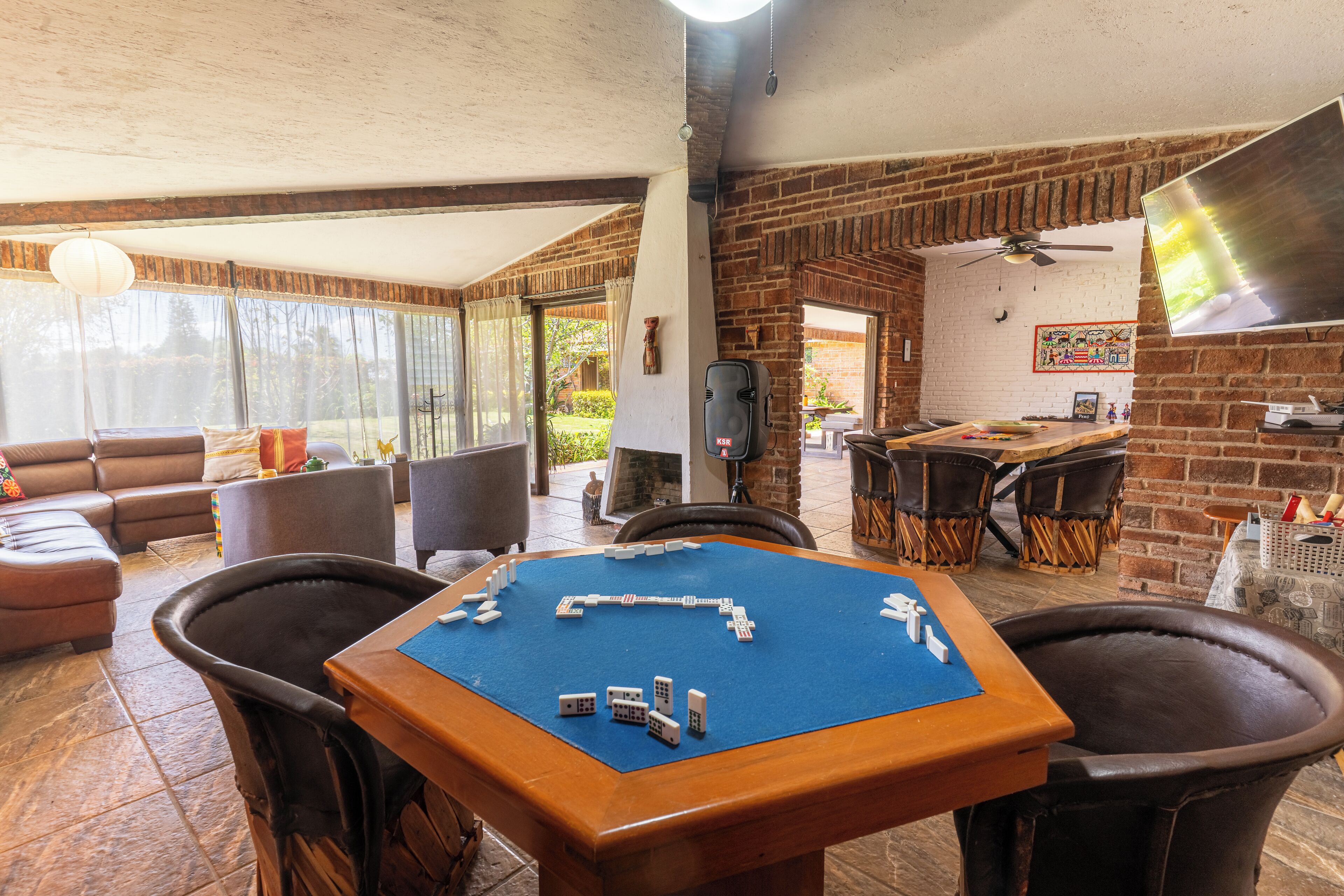Amplia habitación con una gran mesa para jugar a dominó, un sofá y una pared de ladrillo.