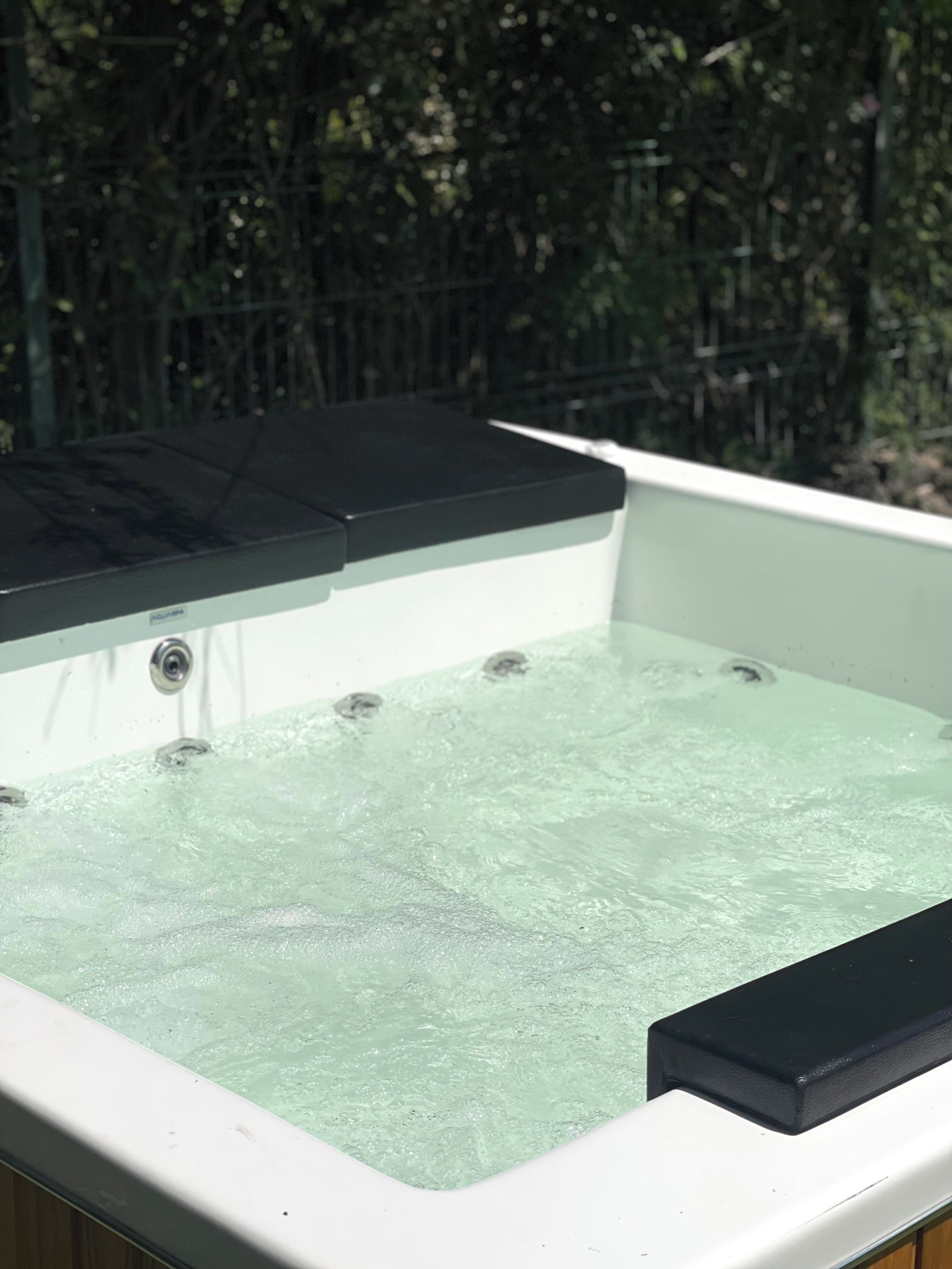 A hot tub with a black lid, surrounded by a white tub and a wooden deck.