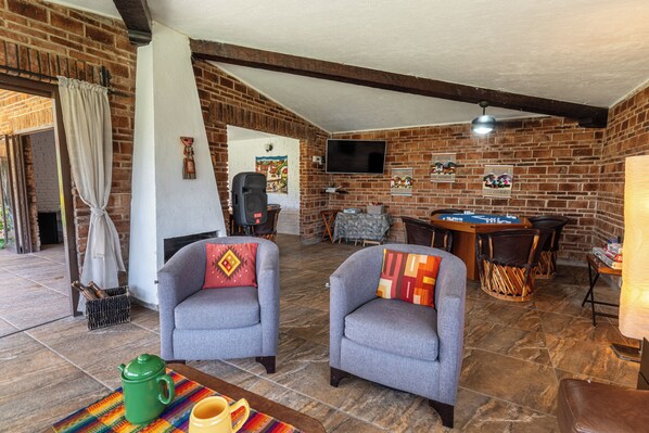 A cozy living room with brick walls, two grey armchairs, a pool table, and a television. - ANANA Casa SK (Ajijic)