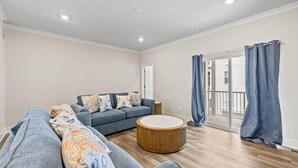 Una sala de estar moderna con un sofá gris, cojines estampados, una mesa de centro de madera y un ventanal con cortinas azules.