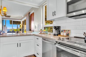A modern kitchen with white cabinetry, a built-in oven, a microwave, and a coffee maker. - Kapalua Bay | Ocean View 4 BR, Sleeps 12 | Car Incl. w/ 6+ Nights | KBV ML-2077 by KBM (Lahaina)
