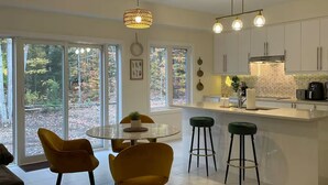 A modern kitchen with white cabinets, a central island with stools, and a dining area with yellow chairs. - Luxury Muskoka Beach Retreat, Games Room & Hot Tub (Gravenhurst)
