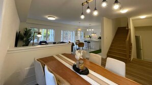 A dining area with a wooden table, white chairs, and a striped runner. There are hanging pendant lights above the table. - Luxury Muskoka Beach Retreat, Games Room & Hot Tub (Gravenhurst)