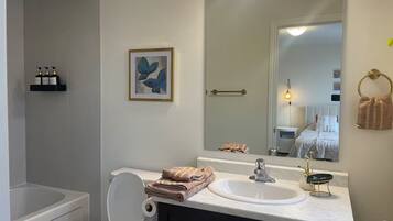 Een badkamer met toilet, wastafel en douche. Er hangt een lijst met kunstwerk aan de muur, een handdoekhouder en een spiegel die de ruimte weerspiegelt.