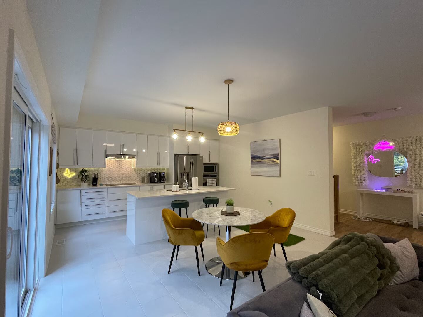 A modern kitchen with white cabinets, a central island, and a dining area with a round table and yellow chairs.