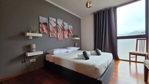 Ein modernes Schlafzimmer mit einem großen Bett, Blick auf die Stadt und Kunstwerken an der Wand.