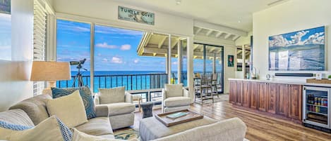 A spacious living area with a view of the ocean, a balcony with a railing, and a kitchen area with wooden cabinets.