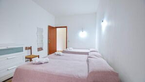 Una habitación de hotel con dos camas, una silla de madera, una mesita, un espejo y una lámpara.