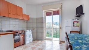 Una cocina compacta con estufa, horno y refrigerador, un comedor con mesa y sillas, y un puerta corrediza de vidrio que da a un balcón.