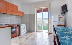 A compact kitchen with a stove, oven, and refrigerator, a dining area with a table and chairs, and a sliding glass door leading to a balcony. - Amazing apartment in Casal Velino with WiFi (Casal Velino)