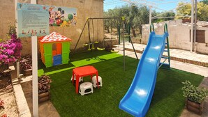 Un área de juegos infantiles con un tobogán, columpios y una casita.