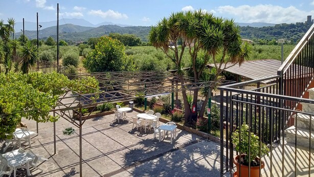 Una terraza con pérgola, mobiliario exterior y vistas a un paisaje exuberante con montañas al fondo.