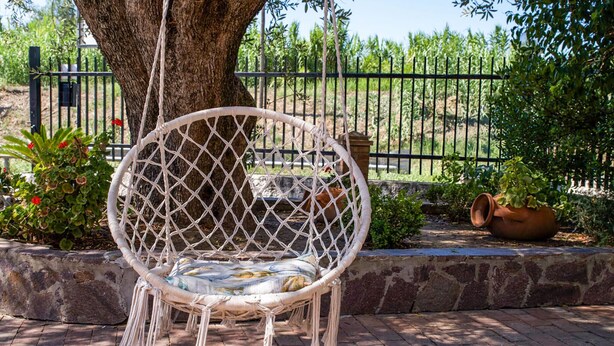 A wicker chair with a cushion, positioned on a brick pathway with a tree and a fence in the background. - Stunning apartment in Casal Velino with WiFi (Casal Velino)