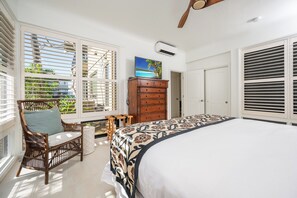Ein Schlafzimmer mit einem großen Bett, einer Holzkommode, einem Korbsessel und Blick auf einen Pool durch das Fenster.