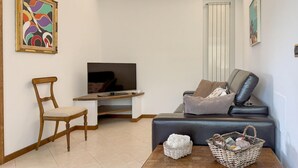 Ein Wohnzimmer mit Fernseher, einem Holzstuhl, einer Couch, einem Couchtisch mit Körben und Kunstwerken an den Wänden.