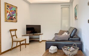 Ein Wohnzimmer mit Fernseher, einem Holzstuhl, einer Couch, einem Couchtisch mit Körben und Kunstwerken an den Wänden.