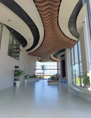 A spacious lobby with a modern ceiling design, large windows, and potted plants. - Beachside 1BR Pool -Salinas del Mar, Santa Marta (El Manantial)