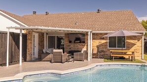 A backyard with a swimming pool, patio furniture, and a covered seating area.