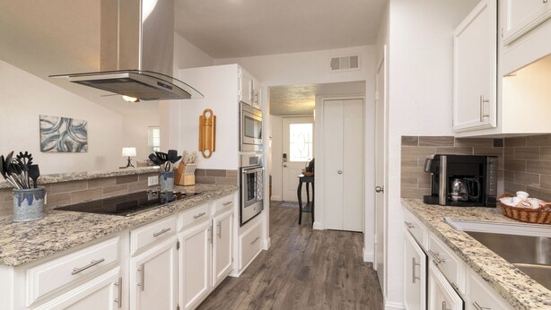 A modern kitchen with white cabinets, granite countertops, stainless steel appliances, and a wooden floor.
