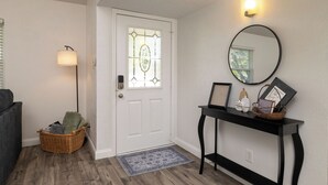 A clean, modern entryway with a white door, a wicker basket, a floor lamp, and a console table with decorative items.