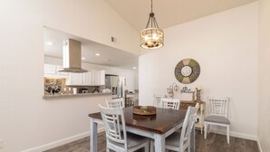 A dining area with a wooden table and white chairs, a hanging light fixture, and a decorative wall piece.