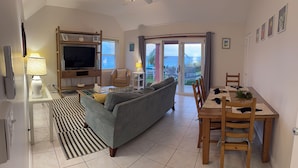 Een woonkamer met een bank, televisie en een eettafel met stoelen.