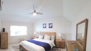 Een slaapkamer met een bed, nachtkastjes, een plafondventilator, een raam en een spiegel.