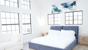 Een slaapkamer met een bed, een witte bank en grote ramen.
