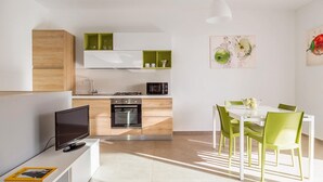A modern kitchen with a dining area, featuring a TV, a microwave, and a dining table with chairs. - Cozy apartment in Ragusa with house sea view (Ragusa)