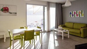A modern living room with a green sofa, a dining table with chairs, and a laptop on a side table. - Cozy apartment in Ragusa with house sea view (Ragusa)