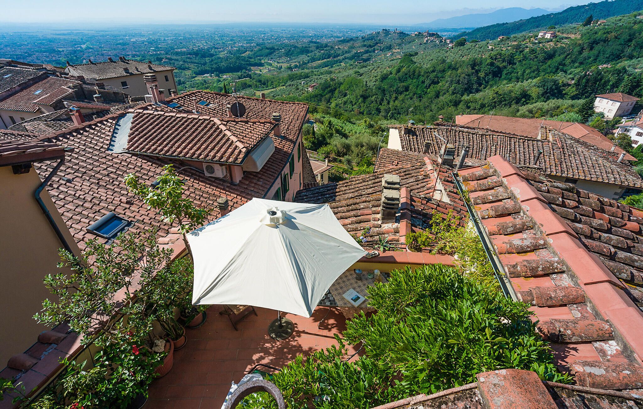 A rooftop terrace with terracotta tiles, potted plants, and a white umbrella.